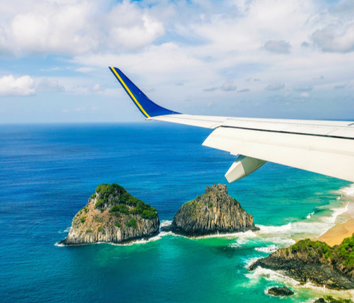 Foto da asa de um avião sobrevoando a ilha Fernando de Noronha