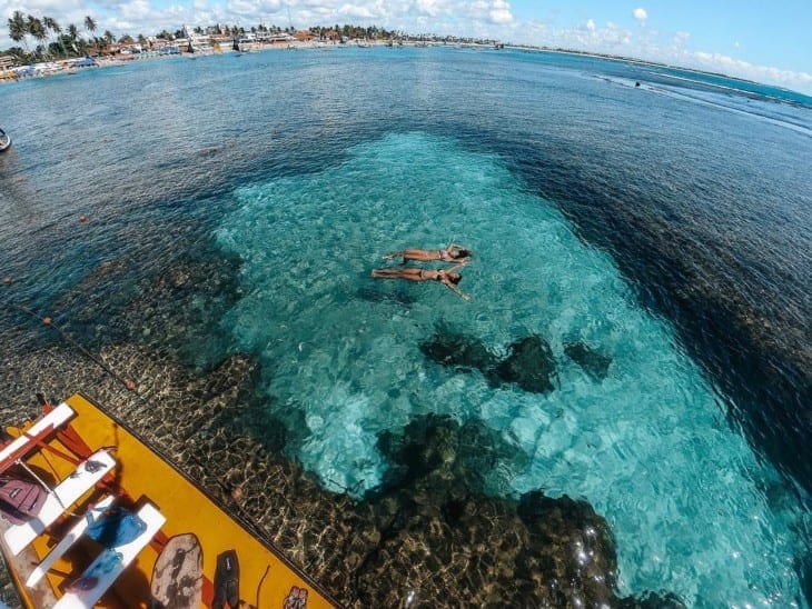 Duas moças nadando sob a água cristalina de uma das piscinas naturais descobrindo o que fazer em porto de galinhas