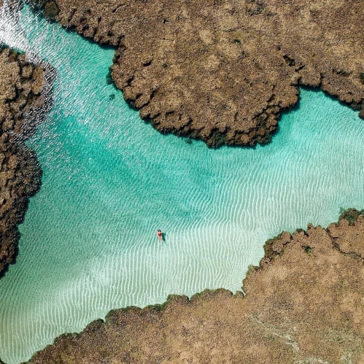 Foto panorâmica de uma imensa piscina natural com uma moça de biquíni vermelho