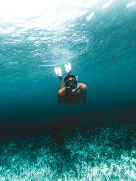 Homem mergulhando num mar azul esverdeado apenas com um snorkel.