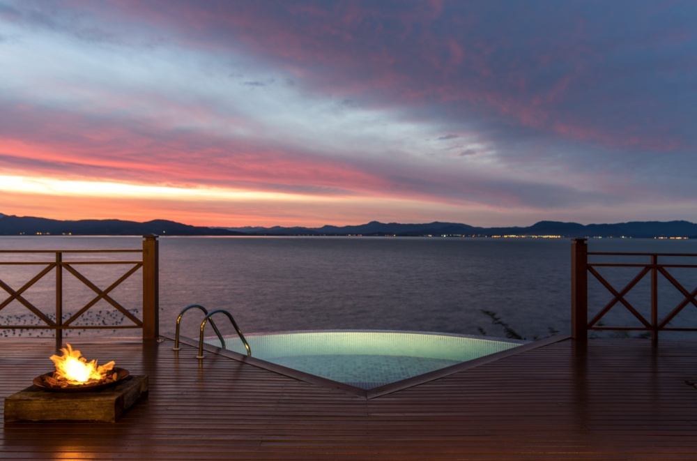 Fogueira sobre um deck de madeira com piscina de frente para o oceano sob um por do céu avermelhado em hotéis e resorts em santa catarina