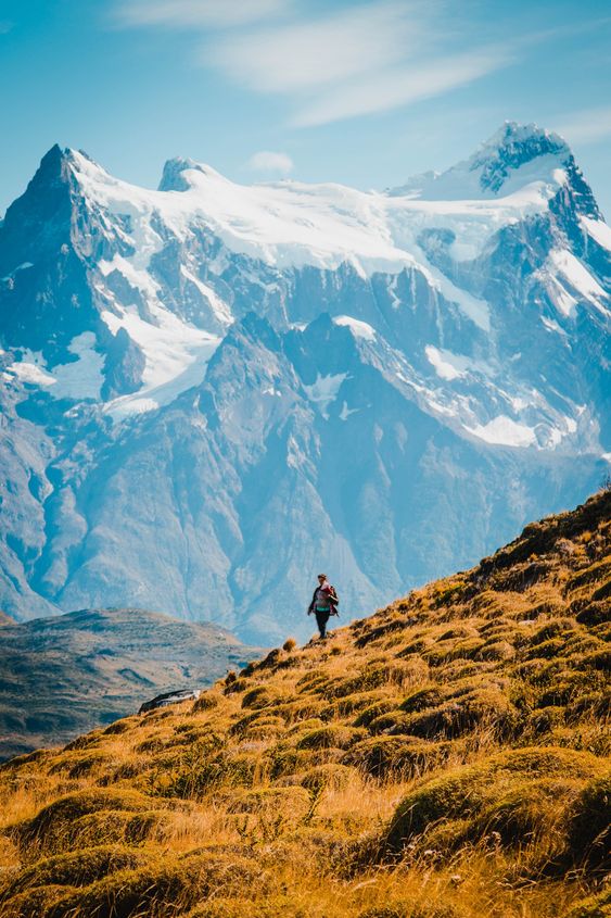 Capo com vegetação amarelada, um pessoa descendo-o com as montanhas da cordilheira dos Andes no fundo em pontos turísticos no chile