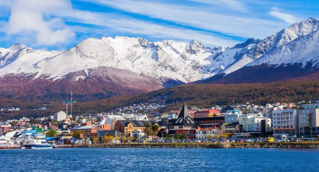 Cidade com montanhas nevadas atrás e um mar azulado a frente em um destino de inverno