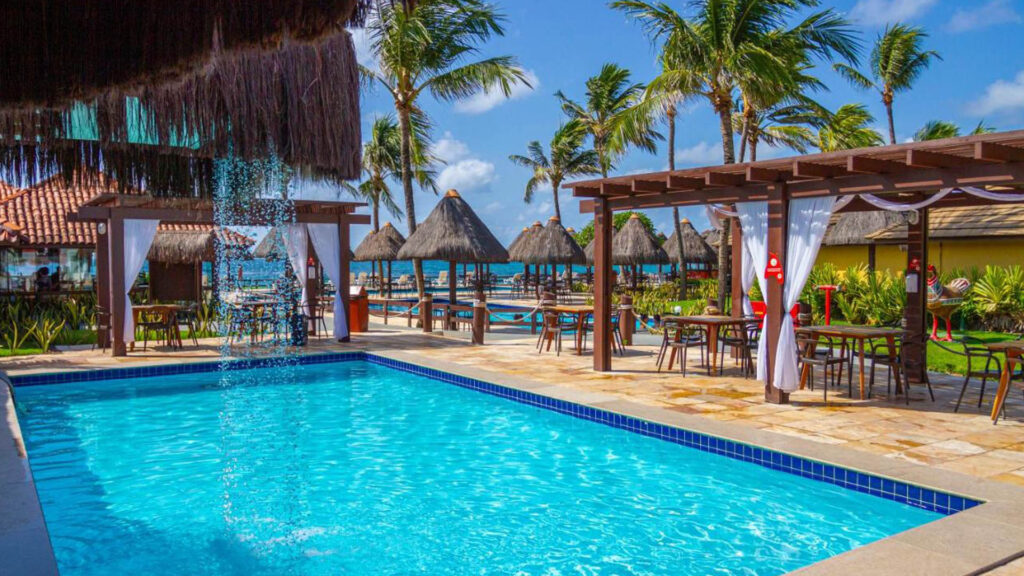 Piscina retangular cercada por estruturas de qualidade feitas da madeira e uma cachoeira artificial em hotel em porto de galinhas beira mar