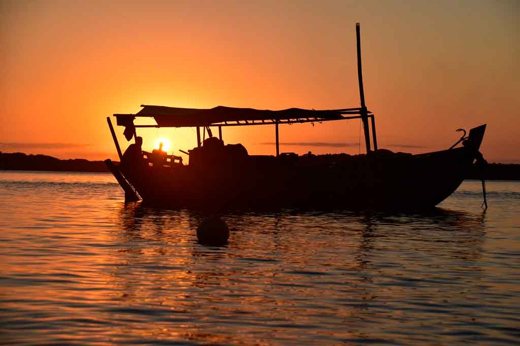 Sombra de barco sob a luz do pôr do sol  no mar alaranjado.