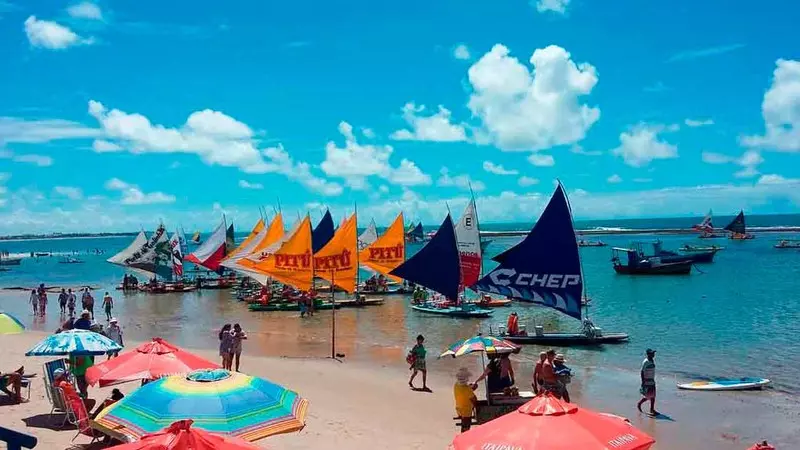 Areia tomada de pessoas e barracas a frente do mar, cheio de pequenas jangadas em pousadas em porto de galinhas no centro