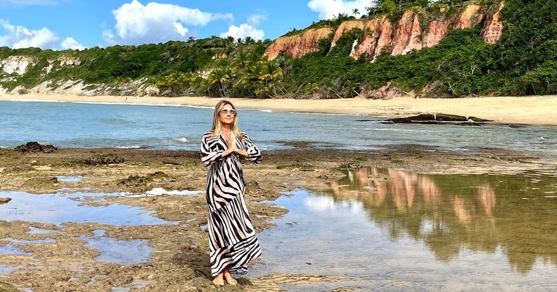 Moça branca de meia idade com vestido preto e branco a frente dos espelhos naturais com as falésias de Trancoso praia do Espelho